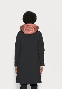 Abrigo exterior negro de corte largo, con una capucha abultada en color rosa dorado. Textura suave y diseño sencillo, con mangas largas y dobladillo recto.