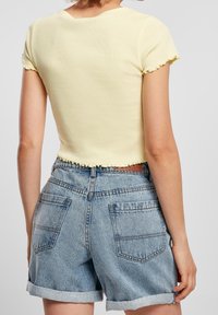 Žlutý ribbed crop top s vlnitými lemy na rukávech, spárovaný s vysokými, světle modrými denimovými šortkami s obrácenými lemy a zadními kapsami.