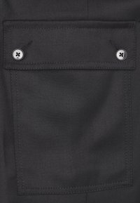 Czarna materiałowa kieszeń z haftowaną obwódką, z dwoma srebrnymi guzikami. Tekstura wydaje się gładka z lekkim połyskiem.