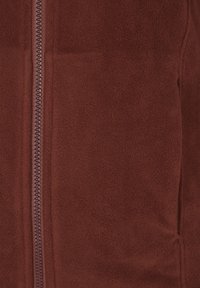 Giacca in pile marrone con una texture liscia, chiusura lampo a tutta lunghezza e tasche laterali. Il tessuto appare morbido e caldo, adatto per il clima fresco.