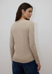 Pull en tricot beige à manches longues, coupe ajustée, poignets côtelés et encolure légèrement arrondie. Associé à un jean bleu en denim.