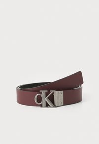 Bordeaux leren riem met een gestructureerde afwerking, voorzien van een zilverkleurige metalen gesp met de opdruk "CK." Vloeiende randen en een klassieke breedte.