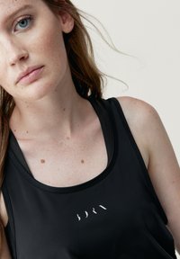 Canottiera sportiva nera con scollatura tonda, tessuto traspirante e un piccolo logo bianco sul davanti. Texture liscia con design aderente.