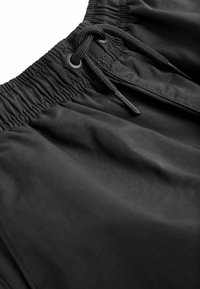Schwarze Badehose aus glattem Stoff mit elastischem Bund und verstellbarem Kordelzug. Besitzt einen dezenten Glanz und eine weiche Textur.