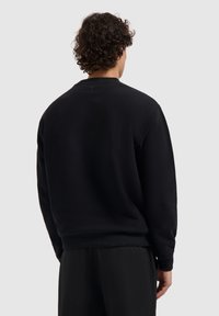 Zwarte katoenen sweatshirt met een ronde halslijn, ribgebreide manchetten en zoom. Soepele textuur, losse pasvorm en een kleine driehoekige accent aan de achterkant.