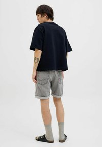 T-shirt en coton noir, coupe décontractée, associé à un short en denim gris retroussé. Chaussures : sandales noires à deux sangles, chaussettes grises. Design simple.