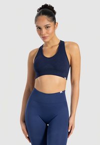 Marinblå ribbad sport-BH med breda axelband, rundad ringning och kort design. Har en liten logotagg vid fållen för branding.