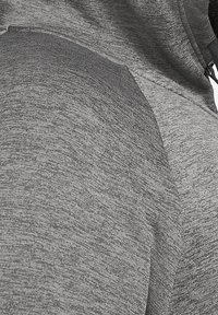 Gros plan sur un tissu chiné gris avec une couture visible et des cordons de capuche sur un sweat-shirt ou un hoodie.