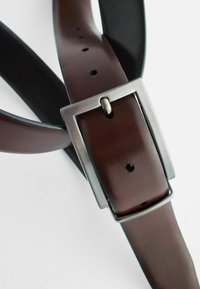 Brown leather belt with a black underside, rectangular silver metal buckle, multiple holes for adjustments, smooth texture, and polished finish.