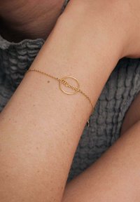 Złota bransoletka z okrągłym zawieszeniem z napisem "Mamuśka" w kursywie. Łańcuszek jest delikatny i ma drobną teksturę.