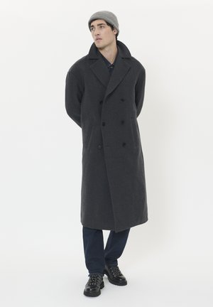 Dark gray, double-breasted wool coat with wide lapels and front pockets, paired with dark pants and black lace-up boots, topped with a gray knit beanie.