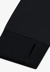 Sort sweaterærmekant med en glat krop og ribbet struktur ved kanten. Har en lille åbning til tommelfingeradgang.