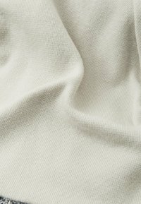 Tessuto lavorato a maglia beige chiaro con una consistenza morbida, caratterizzato da una superficie liscia e cuciture fini. Sottile variazione di colore creano un aspetto delicato.