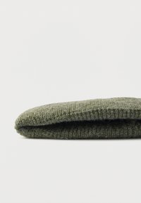 Πράσινο πλεκτό μάλλινο σκουφάκι με μαλακή υφή, στρογγυλεμένο σχήμα και διπλωμένη άκρη. Απλός σχεδιασμός χωρίς επιπλέον μοτίβα ή διακοσμητικά στοιχεία.