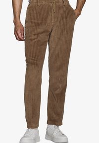 Brune corduroy bukser med lodret ribbing, elastisk talje med snor, sidelommer og tapered ben. Sammen med hvide sneakers.