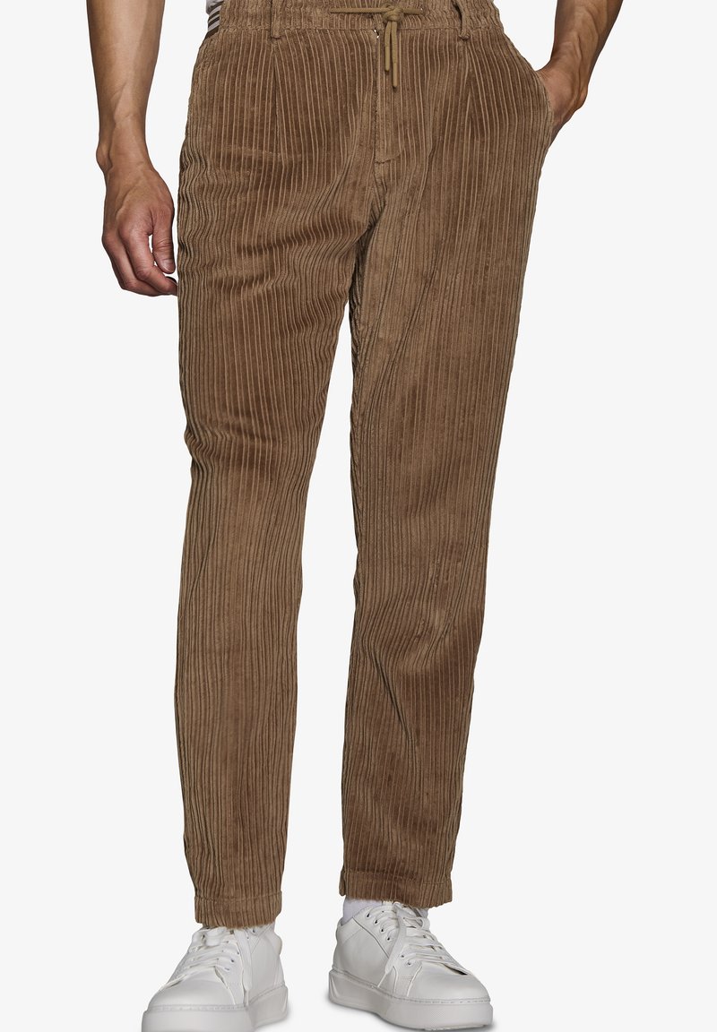 Brune corduroy bukser med lodret ribbing, elastisk talje med snor, sidelommer og tapered ben. Sammen med hvide sneakers.