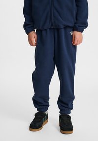 Mörkblå fleece-träningsdräkt med en zip-jacka och byxor med elastisk midja; har en liten logotyp på byxorna och ribbade muddar vid anklarna.