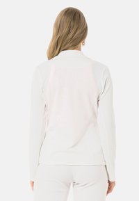 Leichtes, weißes Langarmshirt mit gerippter Textur und einem dezenten reflektierenden Paneel auf der Rückseite. Verfügt über einen Standardkragen und eine taillierte Passform.
