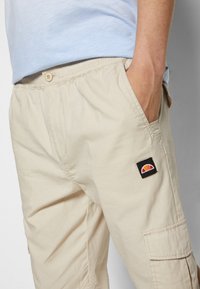 Pantalones cargo caqui hechos de una tela ligera, con bolsillos laterales y un parche negro con un diseño de atardecer colorido. Cintura elástica.