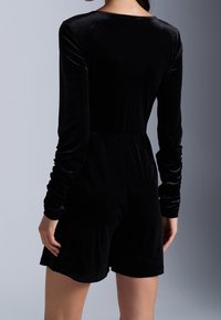 Romper de terciopelo negro de manga larga con un diseño ajustado. Presenta fruncidos en las mangas y un ajuste relajado en la cintura y los pantalones cortos.