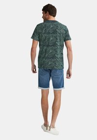 Kortærmet grøn t-shirt med bladmønster, parret med blå denim shorts. Sættet har opnåede kanter og hvide slip-on sko.