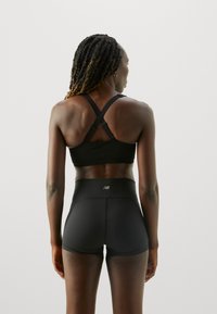 Svart sports-bh med justerbare stropper, kombinert med høyhårede svarte shorts med logo bak, glatt tekstur og tett passform.