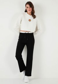 Balts croptops krekls ar tīģera motīvu, savienots ar melniem platajiem biksēm ar aukliņu jostasvietā. Izskatu noslēdz baltas sporta kurpes.