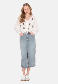 Fehér kötött crop top virágmintával, világoskék farmer szoknyával, amelynek elöl hasíték van, és fehér sneaker cipőkkel, bézs talppal.