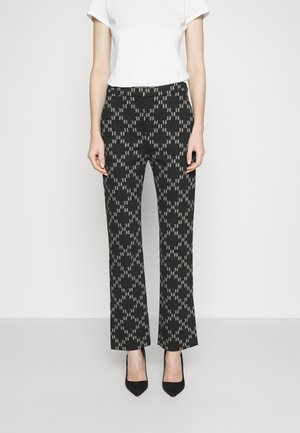 Pantalons noirs à motif en forme de diamant, dotés d'un devant plat, de jambes droites et portés avec des escarpins noirs. Texture de tissu lisse.