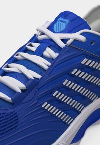 Sinine spordijalats valgete paelte, hõbedaste küljeaktsentide ja K-Swissi logoga keelal, vaadatuna ülalt ja külje suunast.