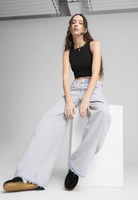 Lichtgrijze wijde jeans met rafelige zomen, gecombineerd met een zwarte aansluitende crop top en zwarte sneakers. Eenvoudig ontwerp, zachte textuur en casual stijl.