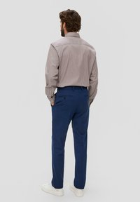 Gestreepte longsleeve shirt in kastanjebruin en wit, gecombineerd met blauwe broek en witte sneakers, gezien vanuit de achterkant.