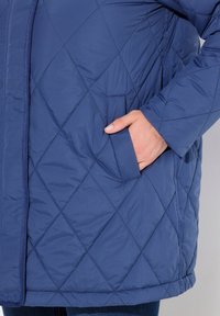 Chaqueta acolchada de color azul marino con patrón de diamantes, bolsillo lateral y textura suave con dobladillo recto.