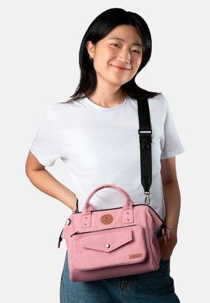 Pink corduroy handbag with short handles, zip closure, and front pocket. Features a detachable shoulder strap and logo patch.