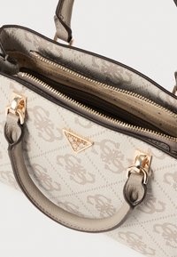 Beige handtas met textuurstof, gouden beslag, dubbele ritsen en een opvallend logo. Heeft een gestructureerd ontwerp en korte handvatten.