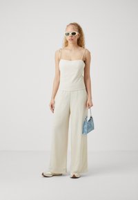 Gai beige lina tank tops ar regulējamiem siksnīēm, apvienots ar plūstošiem, platajiem krēma biksēm. Aksesuāri ietver gaiši zilu rokassomu.