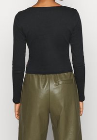 Maglietta nera a maniche lunghe con scollatura quadrata, abbinata a pantaloni in pelle verde oliva con tasca laterale.