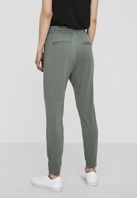 Ljusgröna joggers med elastisk midja, två bakfickor och slim-fit design, parat med vita sneakers.