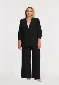Zwarte oversized blazer met knoopsluiting, brede zwarte broek. Glad, lichtgewicht materiaal, met driekwartmouwen en een relaxte pasvorm.