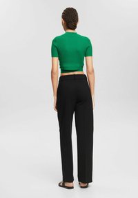 Un haut court à côtes vert associé à un pantalon noir taille haute. La tenue pr ésente des manches courtes, une coupe ajustée et une texture lisse.