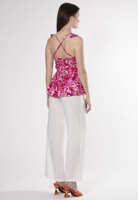 Blomstret peplum-top i levende pink med justerbare stropper, parret med hvide brede bukser. Modellen bærer orange hæle.