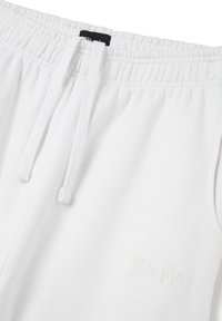 Pantalones de chándal blancos con cintura elástica y cordón. Presentan un sutil logo bordado en la parte frontal, con una textura de algodón suave.