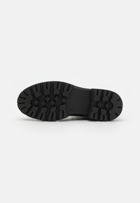 Semelle de chaussure en caoutchouc noire avec un motif de traction texturé, présentant des rainures et des crêtes profondes pour une meilleure adhérence. Conception solide et durable.