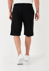 Pantaloni sportivi neri realizzati in morbido tessuto, con una tasca posteriore, una vita elastica e una lunghezza fino al ginocchio.