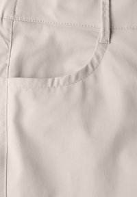 Ljust beige tyg med en slät textur, med en liten fickdetalj och synliga sömmar. Den enkla designen betonar funktionalitet.