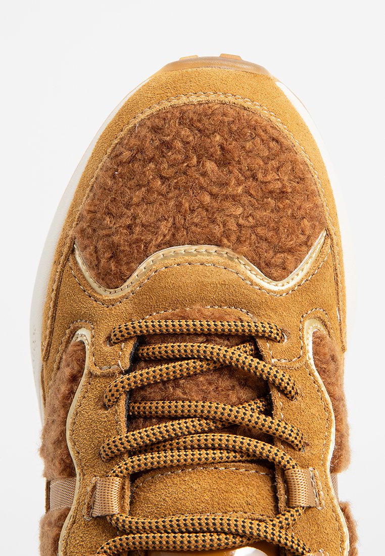 Sneaker met een afgeronde neus, bruin suède materiaal, fuzzy bruine accenten en patroonded veters. Heeft een witte tussenzool en gouden details.