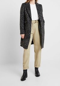 Abrigo de mezcla de lana con estampado de leopardo, hombreras, mangas largas, frente abierto, combinado con pantalones beiges y botines negros.