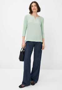 Lichtgroene blouse met lange mouwen en een V-vormige halsopening, gecombineerd met een wijde donkere denim jeans en zwarte mesh flats.