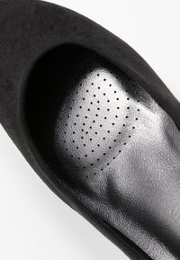 Escarpin noir à talons hauts présentant un extérieur en daim doux et une semelle intérieure en cuir lisse avec un design perforé pour la respirabilité.
