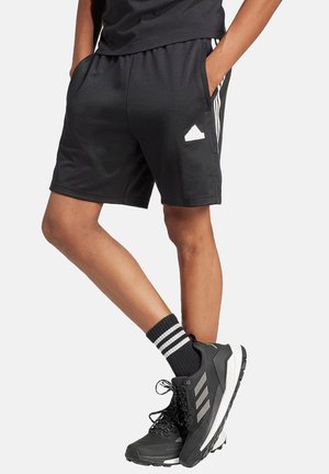 Pantaloni sportivi neri con cintura elastica, tasche laterali e dettagli a strisce bianche. Indossati con scarpe nere e calzini a righe.